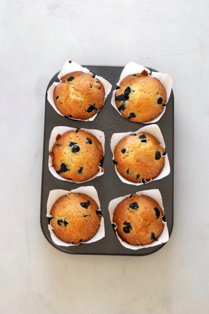 Birds Eye View of 6 jumbo blueberry muffins in the muffin pan on a grey background